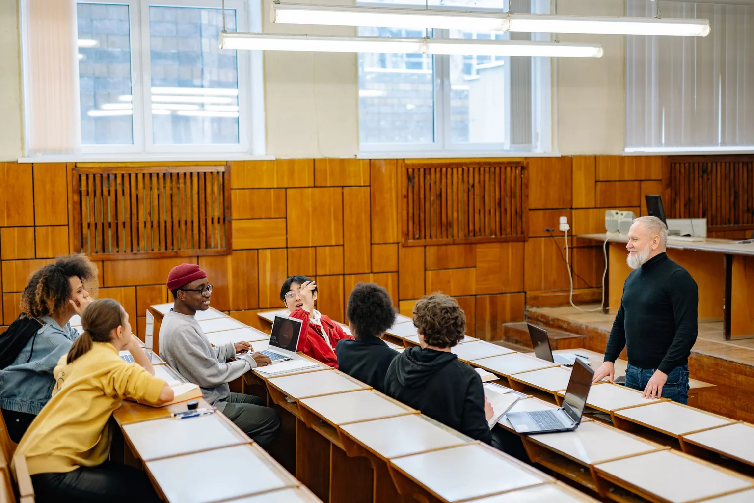 University students and a professor in a lecture hall, with laptops open during class discussion